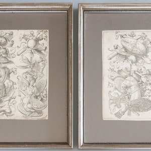 May include: Two framed black and white prints of intricate, detailed drawings of heraldic shields and other decorative elements. The prints are set against a light gray background.