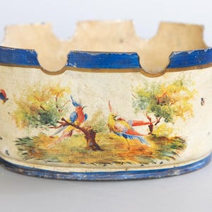 May include: Vintage ashtray with a cream-colored base, blue trim, and gold-colored handles. The ashtray features a hand-painted scene of colorful birds perched on a tree branch. A decorative piece for a home.