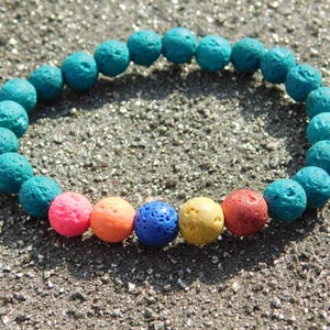 以下が含まれることがあります： ターコイズビーズのブレスレットと、カラフルなアクセントビーズのミックス。 ブレスレットは、ピンク、オレンジ、青、黄色、赤の色合いの丸く多孔質のビーズが特徴です。 ブレスレットは、質感のある砂の表面に表示されています。