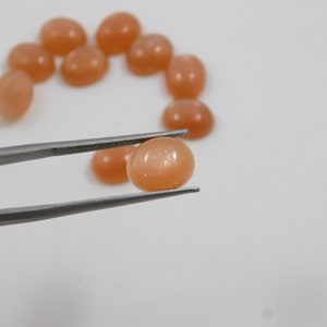 Peach moonstone cabochons, oval-shaped, smooth domed gemstones in peach color; ideal for jewelry making, 5x7–15x20 mm.