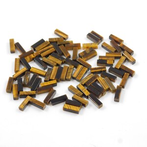 May include: A pile of approximately 50 small, rectangular tiger's eye gemstone beads. The beads are a mix of golden brown and black colours.