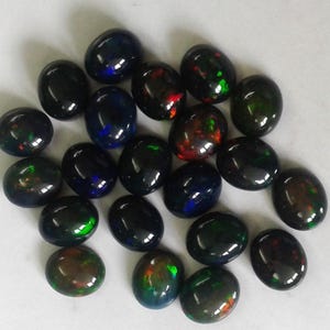 Cluster of small, smooth black Ethiopian opal cabochon ovals on white, dyed stones flashing blue, green, red