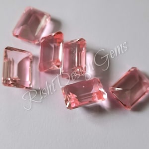 Peut inclure: Six pierres précieuses rectangulaires roses facettées avec un bord biseauté. Les pierres précieuses sont disposées sur une surface blanche. Rishi Design Gems est imprimé sur la surface.