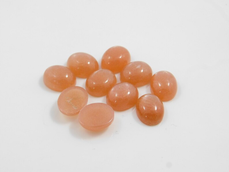 Peach moonstone cabochons, oval-shaped, smooth domed gemstones in peach color; ideal for jewelry making, 5x7–15x20 mm.