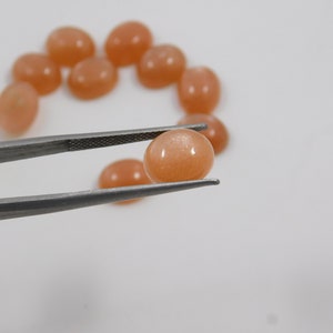 Peach moonstone cabochons, oval-shaped, smooth domed gemstones in peach color; ideal for jewelry making, 5x7–15x20 mm.