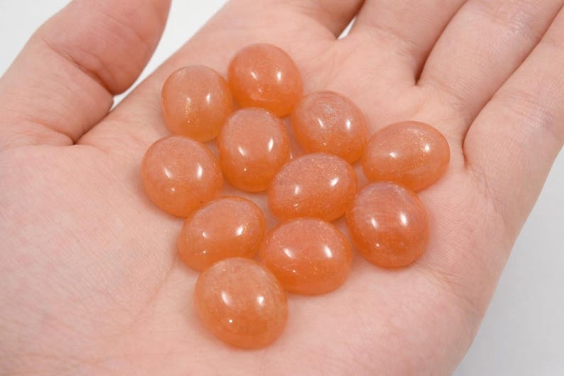 Peach moonstone cabochons, oval-shaped, smooth domed gemstones in peach color; ideal for jewelry making, 5x7–15x20 mm.