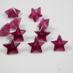 Pode incluir: Dez pedras preciosas de cor vermelha rubi em forma de estrela. As pedras preciosas são facetadas e têm um alto brilho.