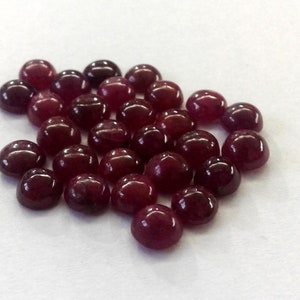 May include: A pile of round, cabochon-cut, ruby red gemstones.