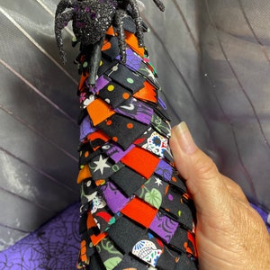 May include: A black and orange fabric Halloween tree with a black spider on top. The tree is made of fabric squares sewn together in a spiral pattern. The fabric has various Halloween-themed prints, including skulls, bats, and candy corn.