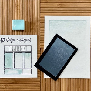 May include: A watercolor pan labeled "Dinner Mint" by Addison &  Gedzyk with a light blue watercolor swatch and a dark blue watercolor swatch.