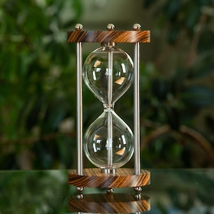 May include: A silver hourglass with a wooden base. The hourglass is filled with clear sand and has a classic design.