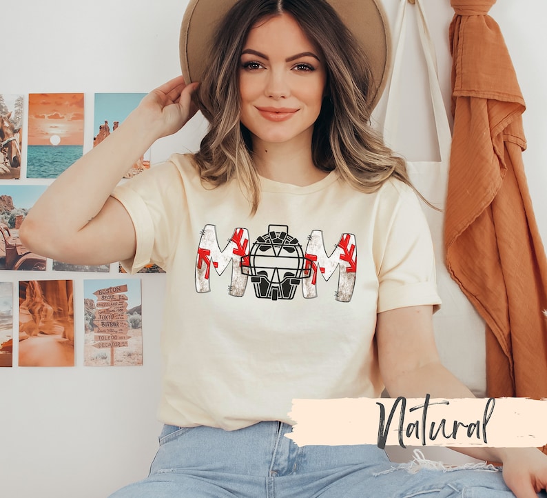 Baseball Shirt features distressed font spelling the word Mom and a Catcher's mask in place of the "o" in Mom.