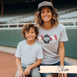 Baseball Shirt features distressed font spelling the word Mom and a Catcher's mask in place of the "o" in Mom.]