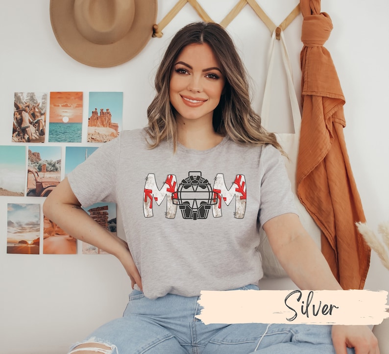 Baseball Shirt features distressed font spelling the word Mom and a Catcher's mask in place of the "o" in Mom.