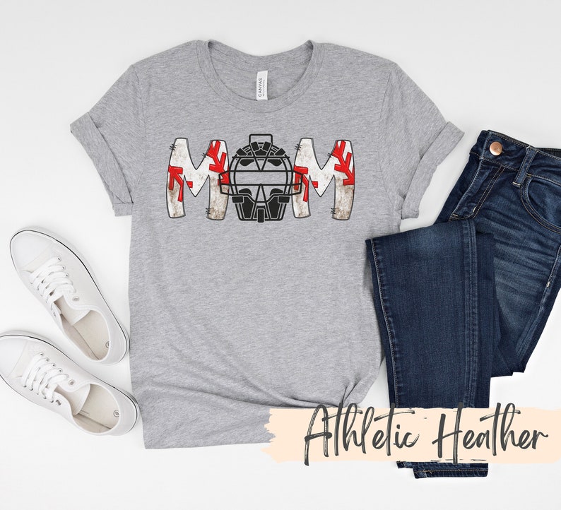 Baseball Shirt features distressed font spelling the word Mom and a Catcher's mask in place of the "o" in Mom.