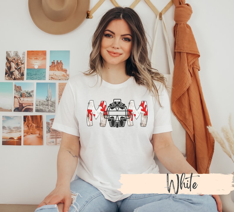 Baseball Shirt features distressed font spelling the word Mom and a Catcher's mask in place of the "o" in Mom.