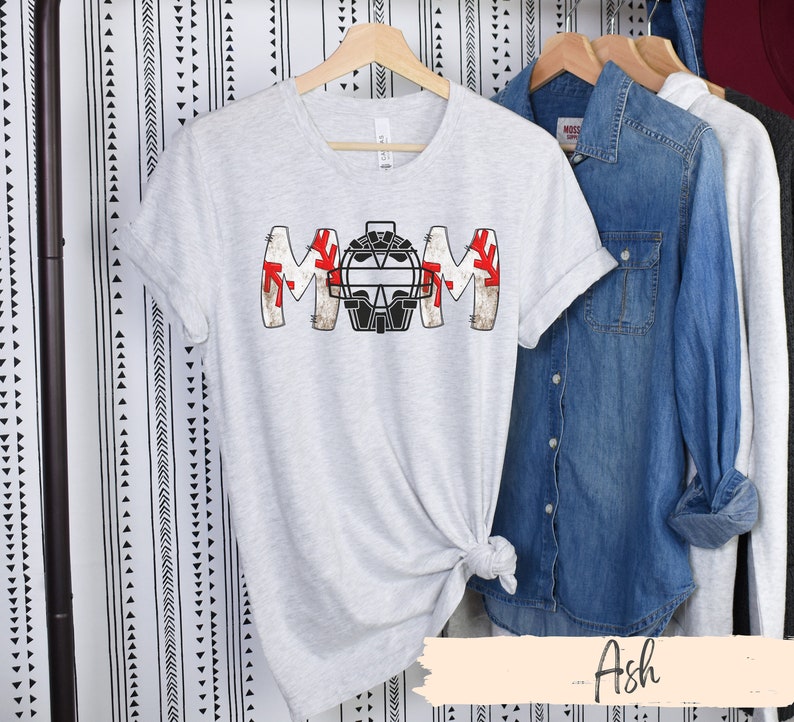 Baseball Shirt features distressed font spelling the word Mom and a Catcher's mask in place of the "o" in Mom.