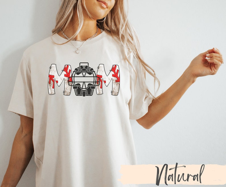 Baseball Shirt features distressed font spelling the word Mom and a Catcher's mask in place of the "o" in Mom.