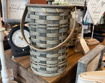 May include: A gray and brown woven basket with a wooden lid and a leather handle. The basket is sitting on a wooden crate. The text "best grandma ever" is visible on a sign in the background.