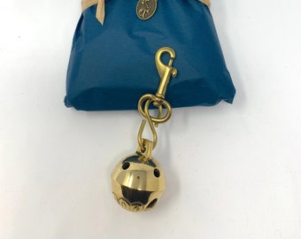 May include: A gold-colored bell with a decorative design and a brass clip attached to a teal blue package wrapped with brown paper and twine. The package has a label that reads "Whimsical Sentimental Things".