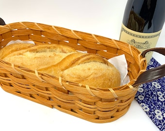 May include: A woven wicker bread basket with a brown leather handle, filled with a loaf of white bread.