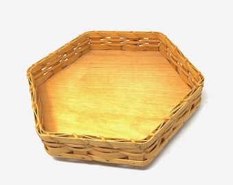 May include: A light brown, hexagonal woven basket with a wooden base. The basket is made of thin, interwoven strips of wood, creating a textured surface. The interior is a lighter shade of wood.