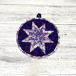 Puede incluir: Posavasos acolchado morado y blanco con un diseño de estrella y un estampado floral.