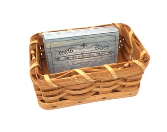 May include: A small, woven wicker basket with a stack of blue and white business cards inside. The cards have a vintage design with the text "Johnson's General Store - Unique Artisanal Finds - Sourced & Crafted in the Midwest".