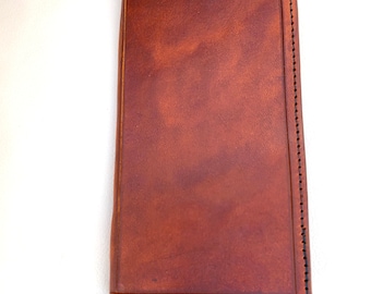 May include: A brown leather wallet with a stitched border. The wallet is closed and lying on a white surface.