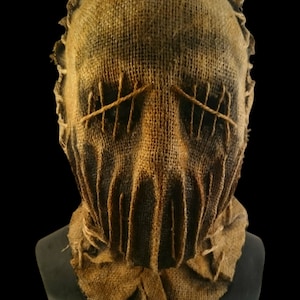 May include: A burlap sack mask with stitched eyes and mouth. The mask is brown and has a rough texture.