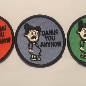 May include: Three round embroidered patches with a cartoon image of a person with a mustache and the text "DAMN YOU ANYHOW". The patches are red, blue, and green.