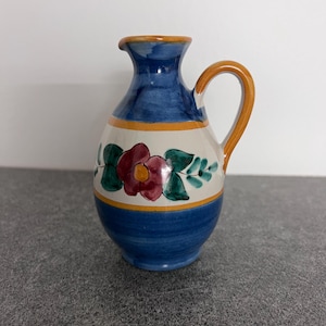 May include: A small blue and white ceramic pitcher with a floral design. The pitcher has a brown handle and a rounded body.