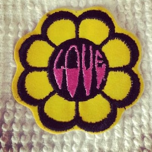 Peut inclure: Une fleur jaune avec un contour noir et un design "LOVE" rose et noir au centre.