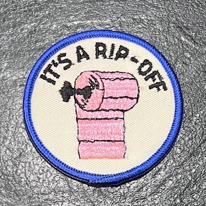 May include: A blue and white embroidered patch with a pink toilet paper roll and the text "It's a rip-off".