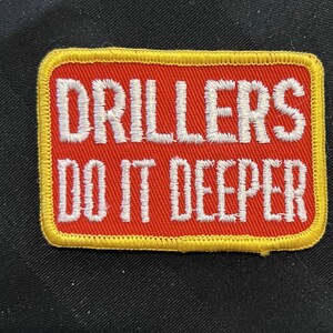 May include: Red and yellow embroidered patch with the text "Drillers Do It Deeper".