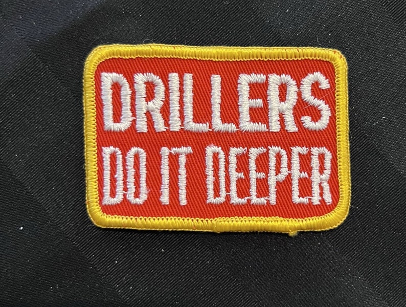 May include: Red and yellow embroidered patch with the text "Drillers Do It Deeper".