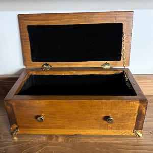 May include: A wooden box with a hinged lid and a black velvet interior. The box has two brass knobs and brass feet. The lid is held closed with a brass chain.
