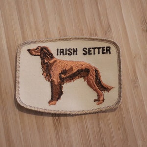 Könnte beinhalten: Ein beigefarbener gestickter Aufnäher mit einem braunen Irish Setter Hund und dem Text "IRISH SETTER" in Braun.