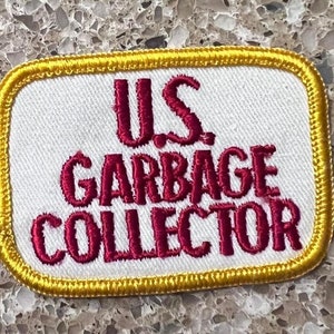 May include: A white embroidered patch with a gold border. The text "U.S. GARBAGE COLLECTOR" is embroidered in red.