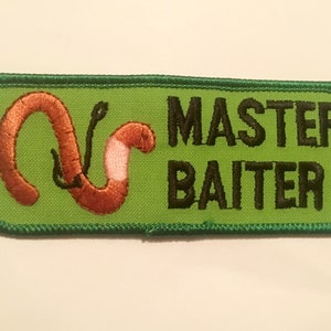 May include: Embroidered patch with a green background and a brown worm on a hook. The text "MASTER BAITER" is in black, block letters. The patch has a green border.