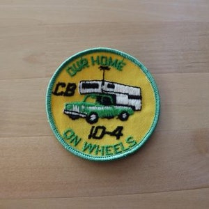 May include: A yellow and green embroidered patch with the text "Our Home On Wheels CB 10-4". The patch features a green car with a white camper on top.