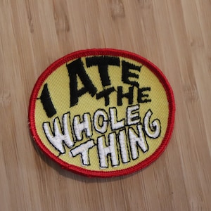 May include: A yellow and red embroidered patch with the text "I ATE THE WHOLE THING" in black and white lettering.