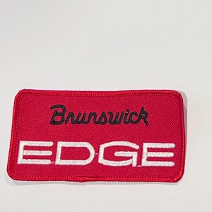 May include: Red fabric patch with white stitching. The patch has black embroidered text that reads "Brunswick EDGE".
