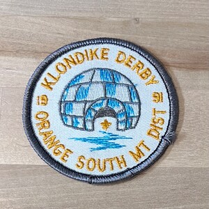 May include: Circular embroidered patch with an igloo design. The patch has an igloo with blue and white stripes, gold text reading "KLONDIKE DERBY" and "ORANGE SOUTH MT DIST", and a grey border.