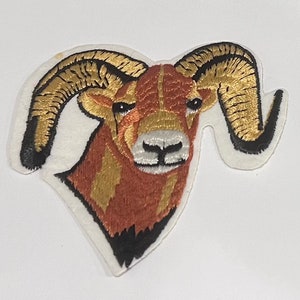 May include: Embroidered patch of a brown and gold bighorn sheep with large curled horns. The sheep's head is facing forward with its mouth closed.