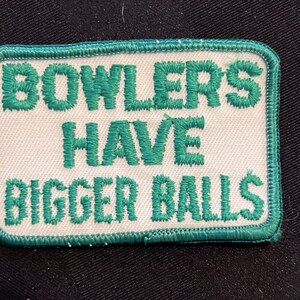 May include: Rectangular patch with the text "BOWLERS HAVE BIGGER BALLS" in green embroidered letters on a white background. The patch has a green border.