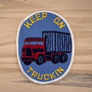 May include: A blue and white embroidered patch with a red truck and the text "Keep on Truckin'" in yellow.