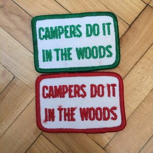 May include: Two embroidered patches with white fabric and red and green borders. The top patch has green text that reads "Campers Do It In The Woods". The bottom patch has red text that reads "Campers Do It In The Woods".