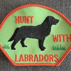 May include: Green embroidered patch with an orange border. The patch features a black Labrador Retriever standing on a green field with the text "Hunt with Labradors" in orange.