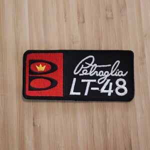May include: Black and red embroidered patch with a white crown and the text "Belagia LT-48".